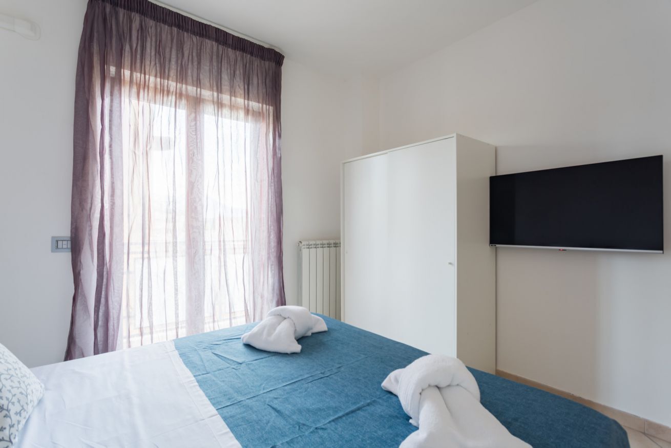 A hotel room with a bed, a wardrobe, a television, and a window with curtains.