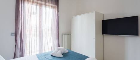 A hotel room with a bed, a wardrobe, a television, and a window with curtains.