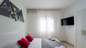 Hotellihuone, jossa on sänky, taulutelevisio, vaatekaappi ja taulu seinällä.