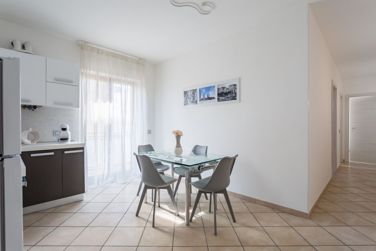 A modern kitchen with a dining area, featuring a glass table, chairs, and a refrigerator.