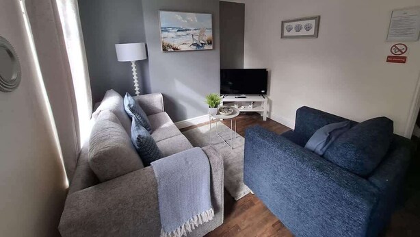 A living room with a grey sofa, a blue sofa, a TV, and a lamp. - 3 Bedroom Home Near Beach & Attractions (Great Yarmouth)