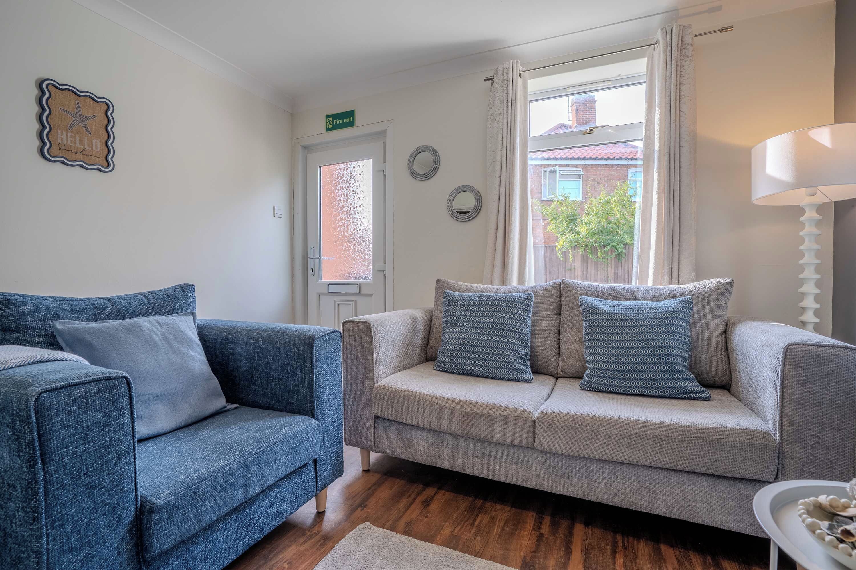 A living room with a blue sofa, a grey sofa, and a white side table with a lamp.