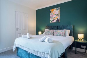 A bedroom with a bed, two bedside lamps, a door, and a painting on the wall. - 3 Bedroom Home Near Beach & Attractions (Great Yarmouth)