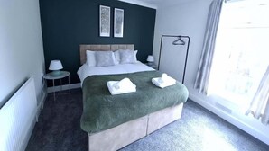 A hotel room with a bed, bedside tables, a lamp, a window with curtains, and a view of the outside. - 3 Bedroom Home Near Beach & Attractions (Great Yarmouth)