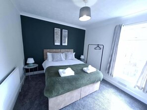 Ein Hotelzimmer mit Bett, Nachttischen, einer Lampe, einem Fenster mit Vorhängen und Blick ins Freie.