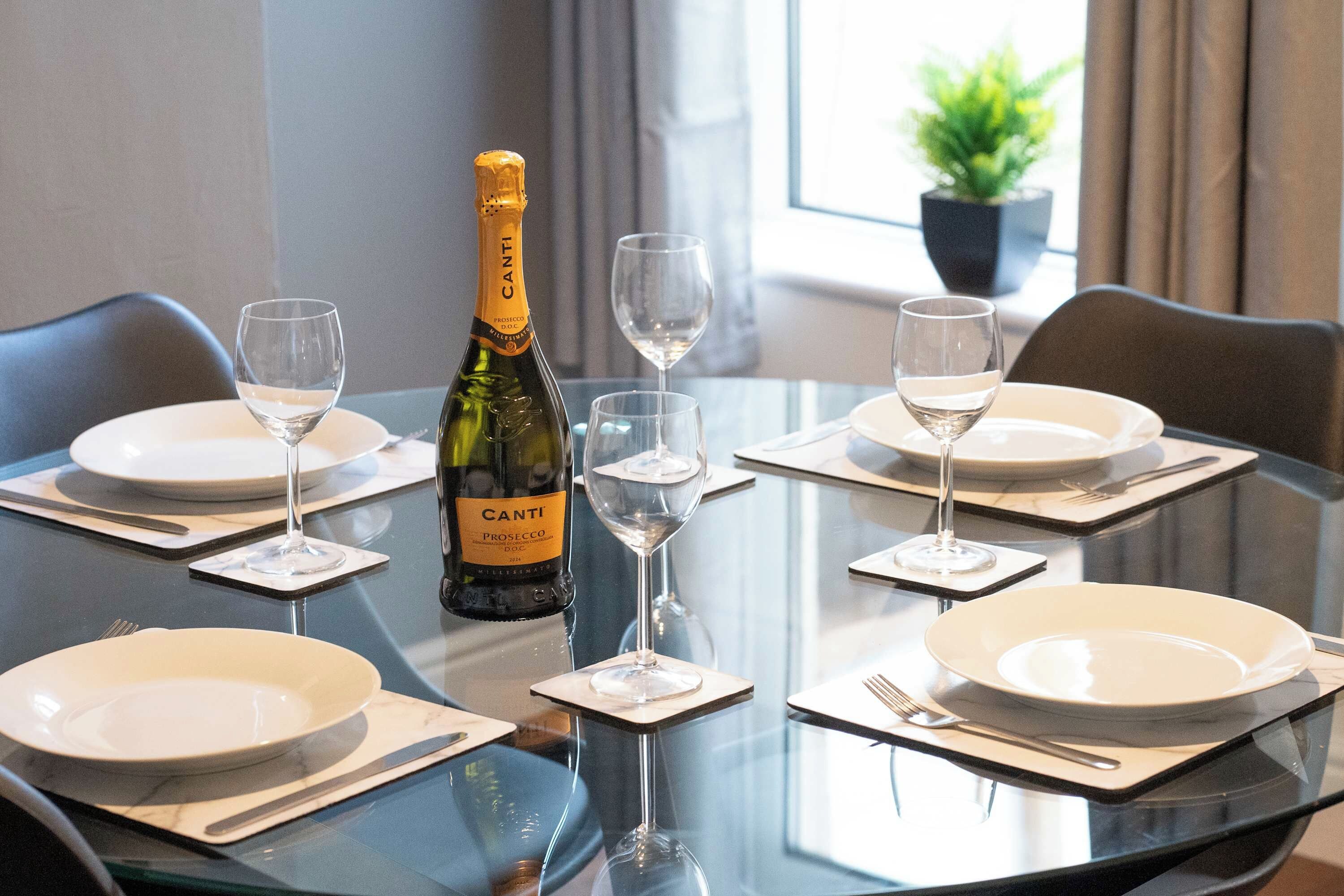 A table set for four with a bottle of Canti Prosecco DOC, four wine glasses, and plates.