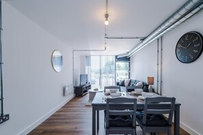 Un espace de repas moderne avec une table dressée pour deux personnes, une horloge au mur et une vue par la fenêtre.