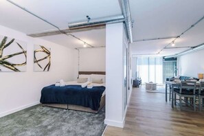 A modern hotel room with a bed, a desk, and a dining area.