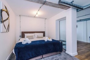 A modern hotel room with a bed, a desk, and a view of the outside.