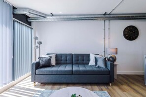 A modern living room with a grey sofa, a round coffee table, and a wall clock.