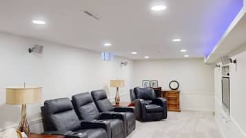 Een kamer met een modulaire bank, twee fauteuils, een klein houten kastje en een flatscreen televisie die aan de muur is bevestigd.