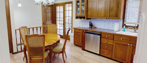 Una cocina con armarios de madera, lavavajillas y un comedor con mesa y sillas.