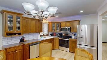 A modern kitchen with wooden cabinets, a central island, a dining table, and a chandelier.