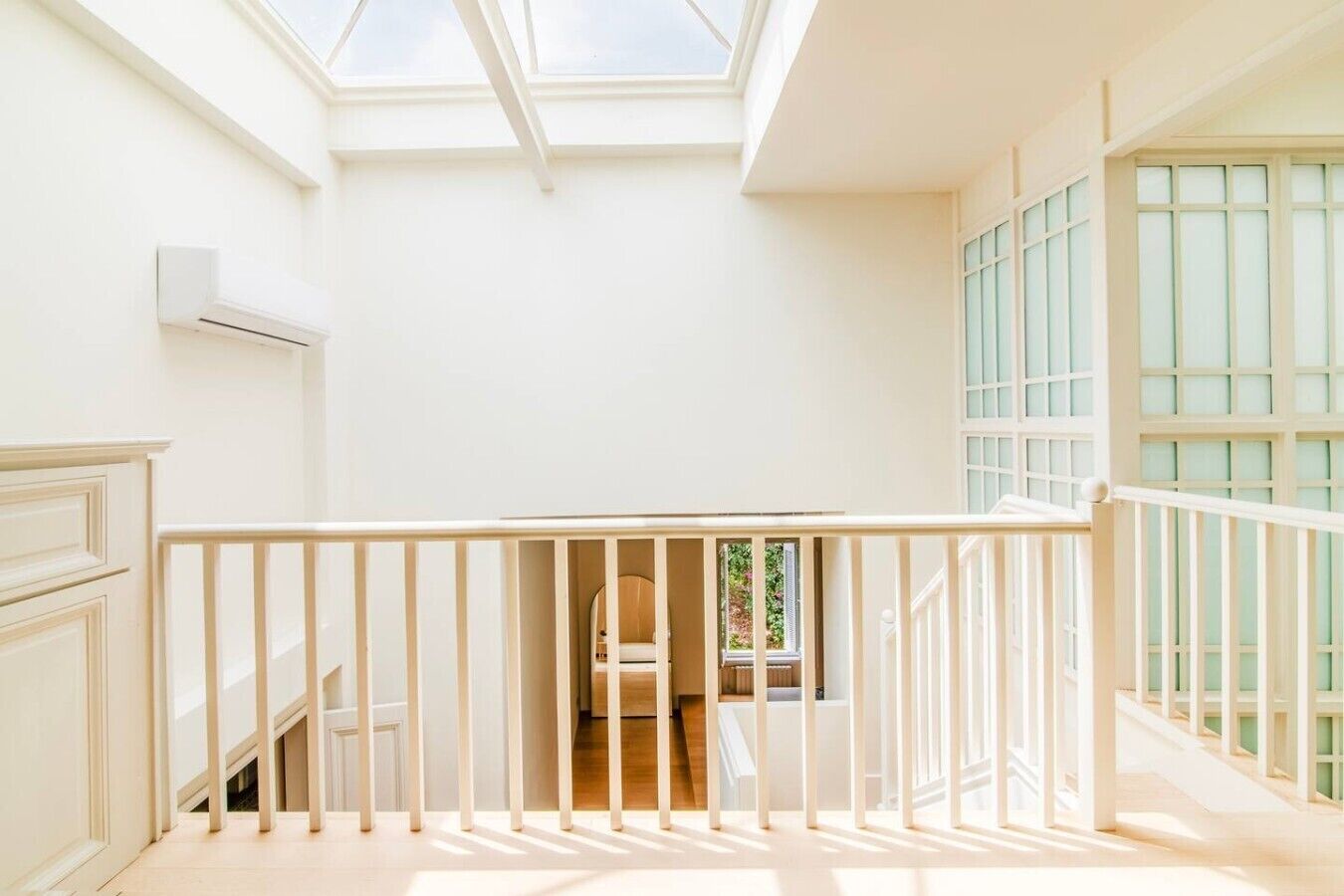 A bright room with a skylight, white walls, a staircase, and a view of greenery outside.