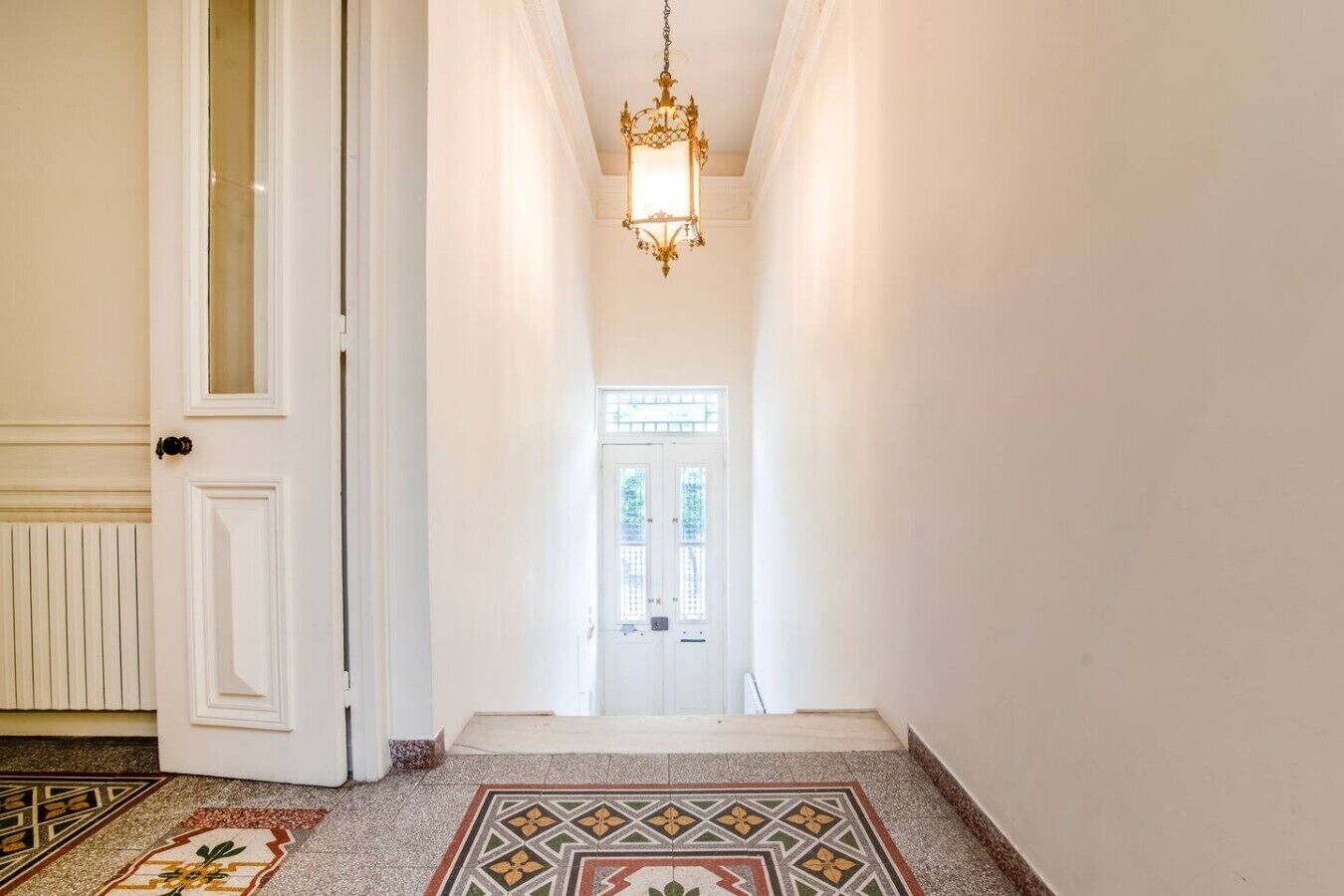 A hallway with a patterned floor, a chandelier, and a door with a glass panel.