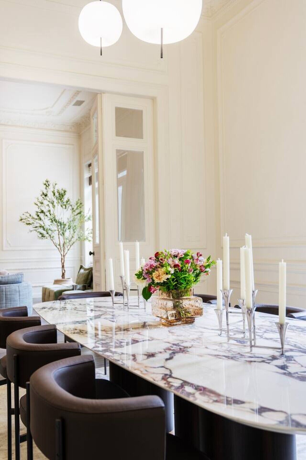 A dining room with a marble table, candles, and a vase of flowers.