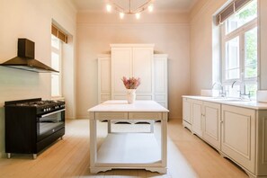 A kitchen with a stove, oven, white cabinets, a table with a vase, and a window.