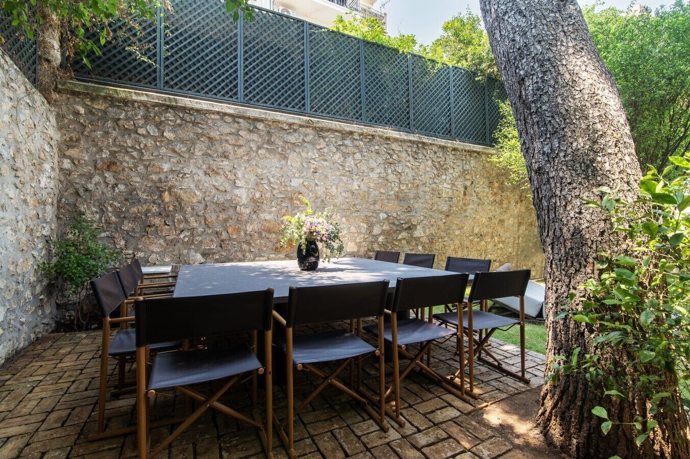 An outdoor patio with a stone wall, a metal fence, and a large tree.
