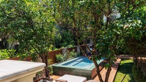 A private outdoor pool area with a hot tub, wooden deck, and lush greenery.