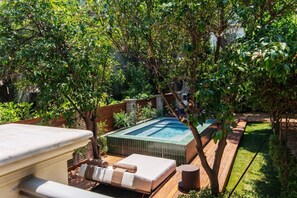 A private outdoor pool area with a hot tub, wooden deck, and lush greenery.