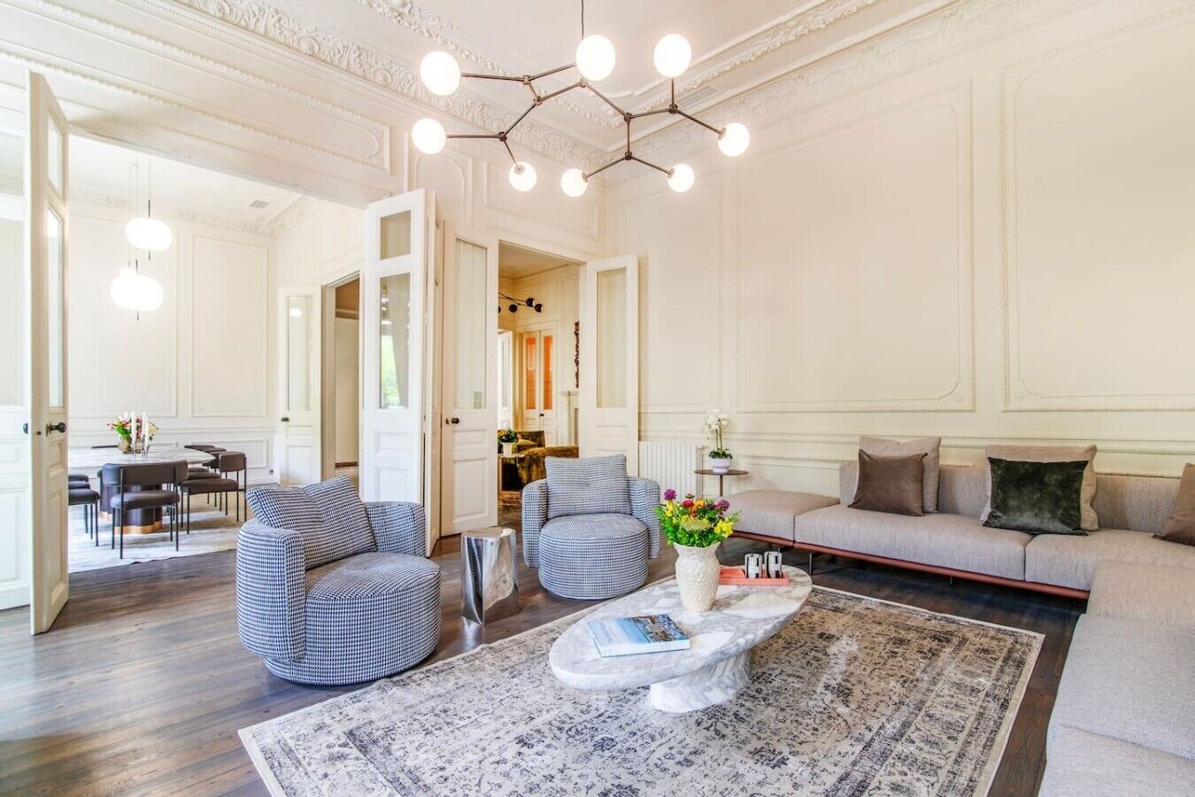 A spacious living room with a round coffee table, two armchairs, a sofa, and a dining area with a table and chairs.