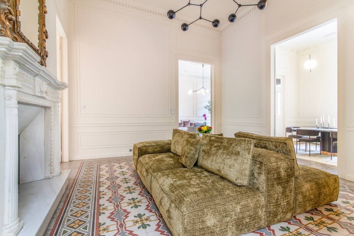A spacious room with a patterned floor, a sofa, a fireplace, and a dining area visible through an open door.