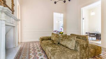 A spacious room with a patterned floor, a sofa, a fireplace, and a dining area visible through an open door.