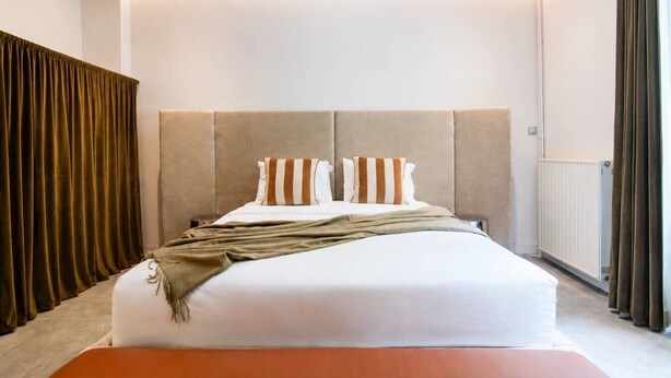Une chambre d’hôtel avec un grand lit, une tête de lit, une table de chevet et des rideaux.