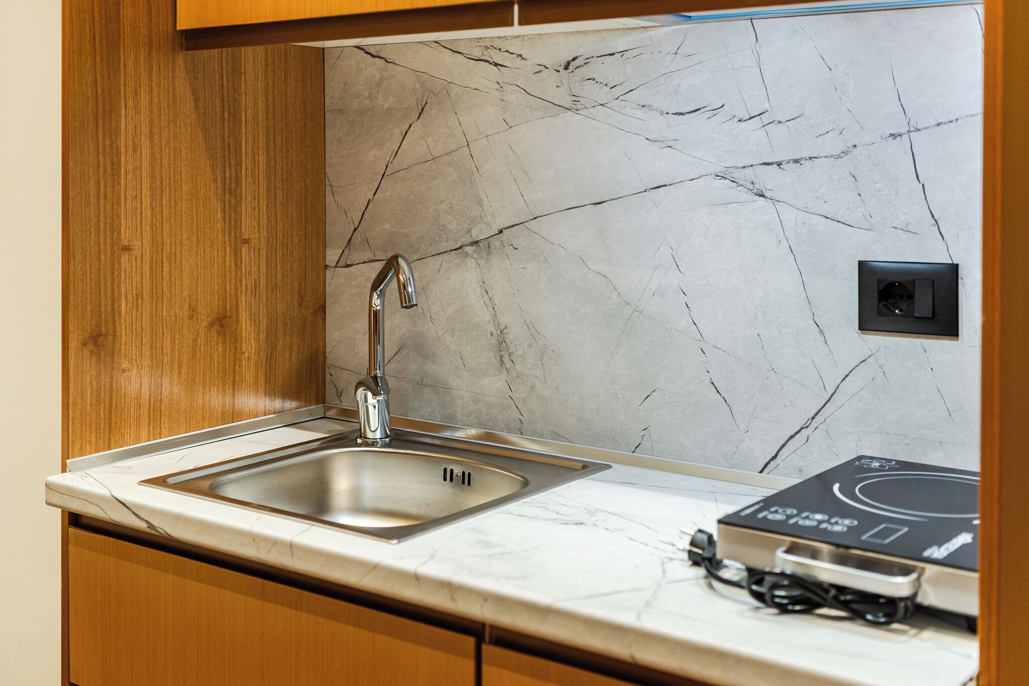 A kitchen with a marble backsplash, a stainless steel sink, wooden cabinets, and a built-in induction cooktop.