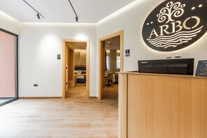 Zona de recepción de un hotel con un mostrador de madera, una computadora Lenovo y un cartel en la pared que dice 'ARBO'.