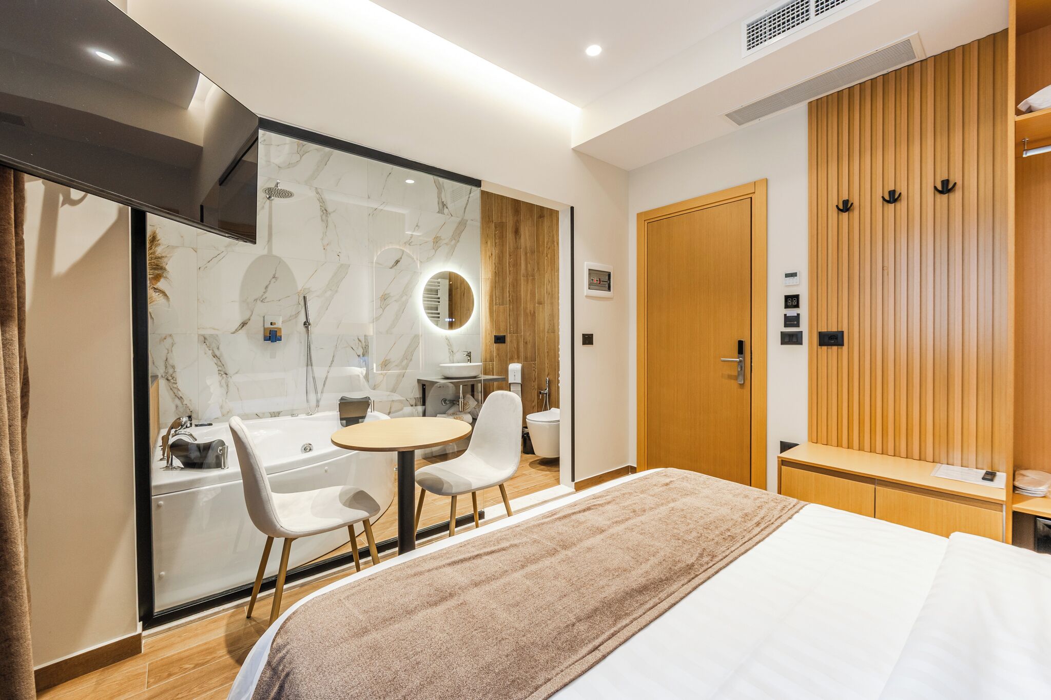 Habitació d'hotel moderna amb un llit gran, zona de seients amb una taula i cadires, bany amb banyera i mirall, i un armari de fusta.