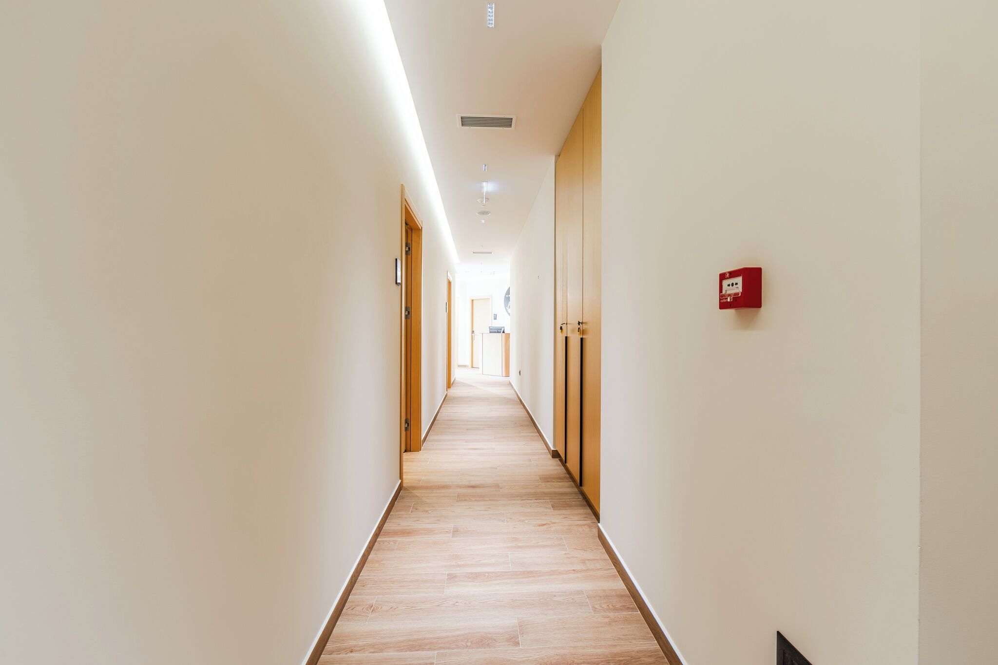 Un long couloir étroit, doté d’un plancher en bois et de murs blancs.