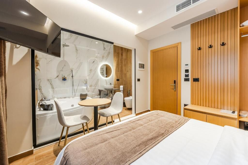 Une chambre d’hôtel moderne équipée d’un lit, d’une salle de bain avec douche, d’un meuble-lavabo et d’un coin salon avec des fauteuils.