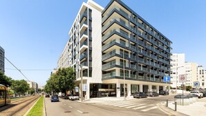 A modern multi-story building with a prominent entrance, a visible restaurant sign, and a tram line nearby. - GuestReady-Charming Gaia Retreat with Balcony (Vila Nova de Gaia)