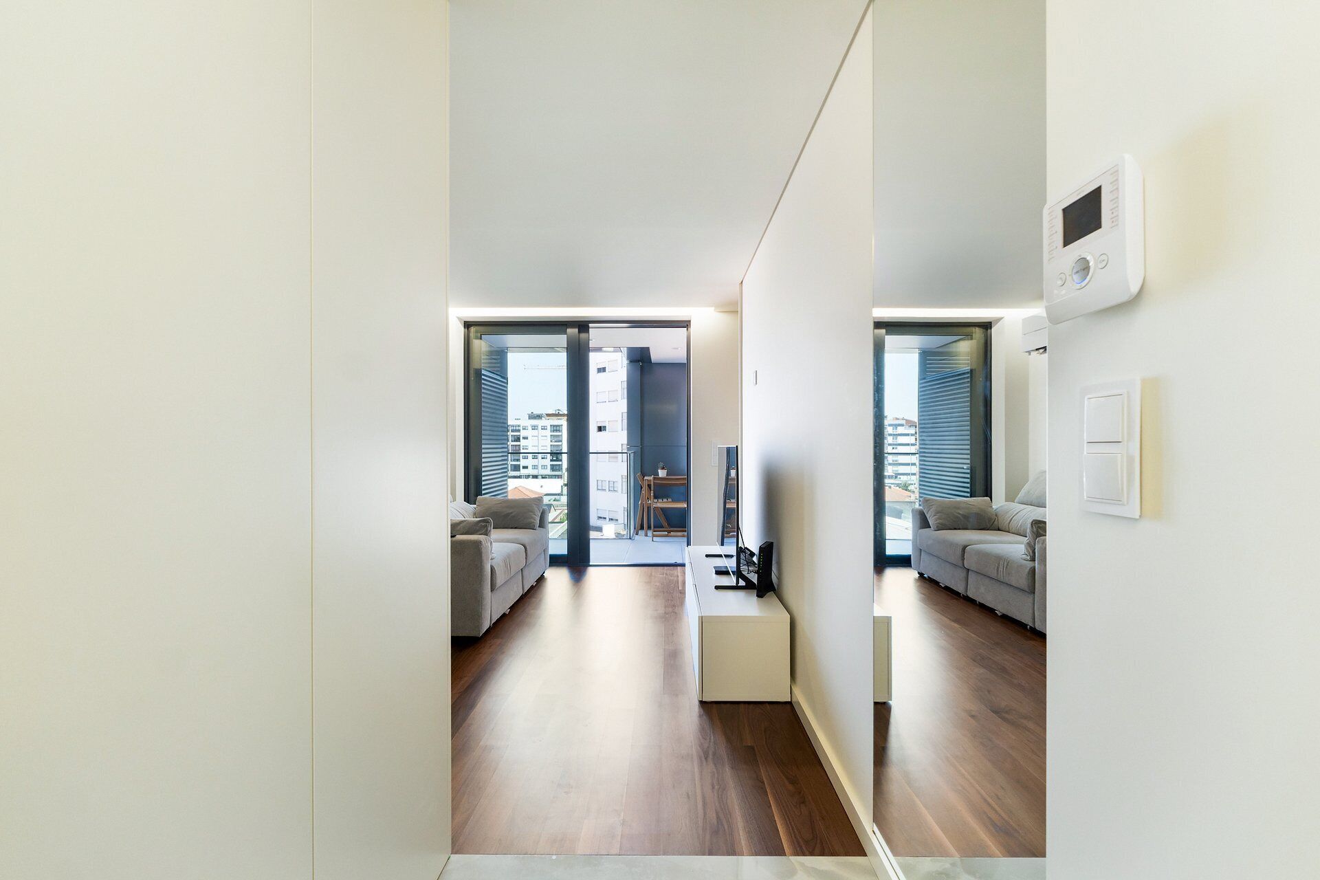 A modern apartment with a minimalist design, featuring a sofa, a small table, and a view through the glass doors.