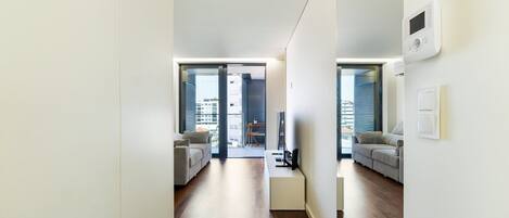 A modern apartment with a minimalist design, featuring a sofa, a small table, and a view through the glass doors.
