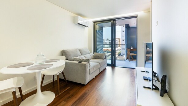 A modern living room with a sofa, a dining table, and a TV. - GuestReady-Charming Gaia Retreat with Balcony (Vila Nova de Gaia)