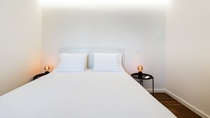 A minimalist hotel room with a single bed, two bedside tables with lamps, and a wooden floor. - GuestReady-Charming Gaia Retreat with Balcony (Vila Nova de Gaia)