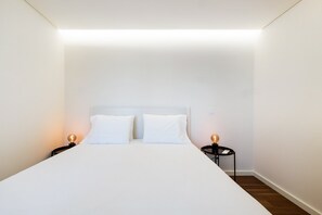 Ein schlicht eingerichtetes Hotelzimmer mit einem Einzelbett, zwei Nachttischen mit Lampen und Holzboden.