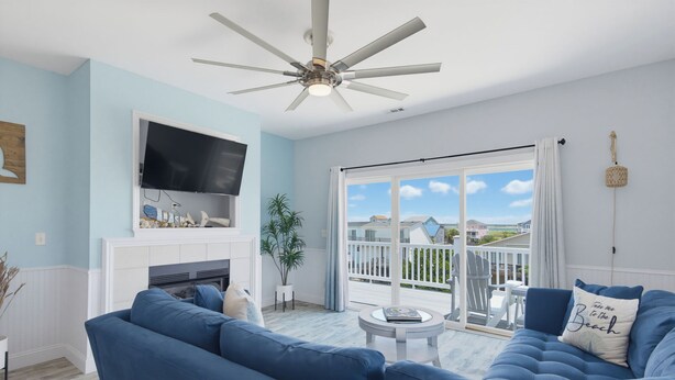 Un salon avec un canapé bleu, une cheminée, un ventilateur de plafond et une vue sur l’extérieur.