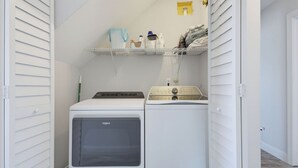 Une buanderie équipée d’un lave-linge et d’un sèche-linge à chargement frontal, d’une étagère contenant des produits de nettoyage et d’une porte donnant sur une autre pièce.