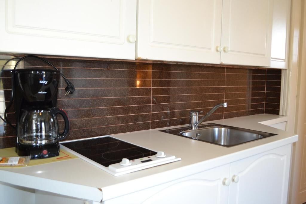 A kitchen with white cabinets, a black coffee maker, a sink, and a stovetop.