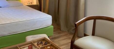 Een hotelkamer met een bed, een nachtkastje van hout met een lamp, een stoel en een bijzettafeltje met diverse spullen.