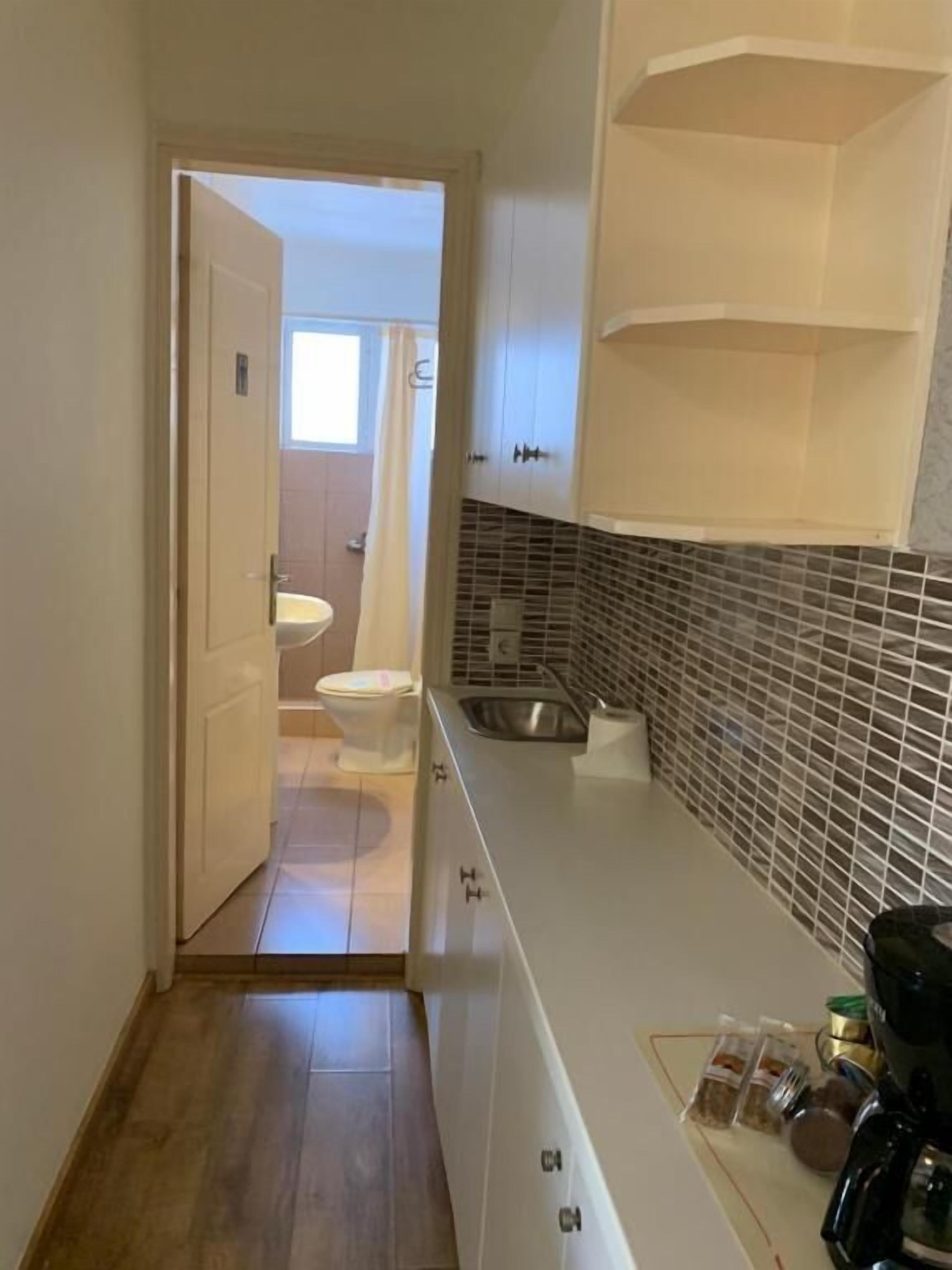 Ein schmales Entree führt zu einem Badezimmer mit Toilette und Waschbecken, einer Küchenzeile mit Waschbecken und Schränken sowie einer gefliesten Spritzwand.