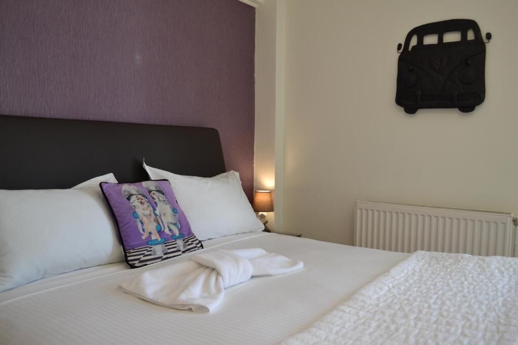A neatly made bed with white linens, a purple pillow with a cartoon character, and a black headboard.