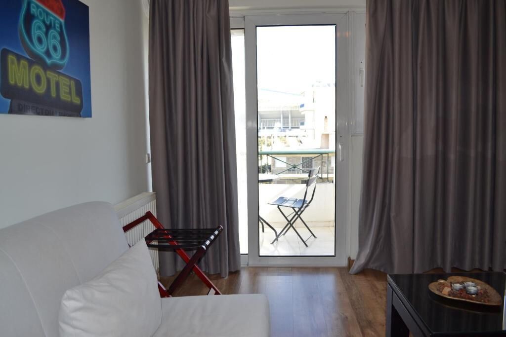 A room with a white sofa, a small table with a tray of snacks, a folding chair, and a view of a balcony with outdoor furniture.