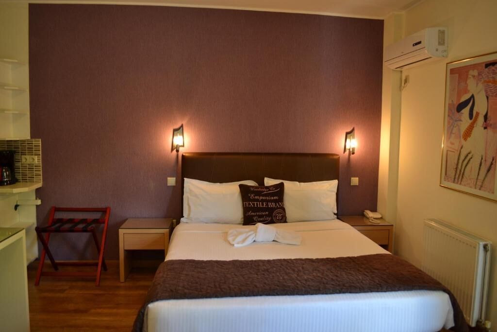 Hotellihuone, jossa on suuri sänky, kaksi yöpöytävalaisinta, yöpöytä, puinen tuoli ja patteri.