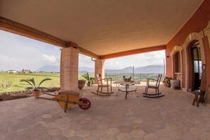 A covered patio with hexagonal tiles, wooden rocking chairs, a small table, and potted plants. - Homerez - Spacious Villa with Pool in Segni (Segni)