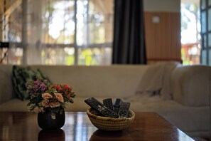 Una sala de estar con un sofá, una mesa con un cesto de controles remotos y un florero con flores.