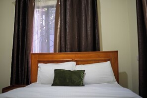 Una cama con cabecera de madera, ropa de cama blanca y almohada verde.